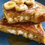 Decadent banana stuffed French toast topped with fresh banana slices, whipped cream, and maple syrup, perfect for brunch.